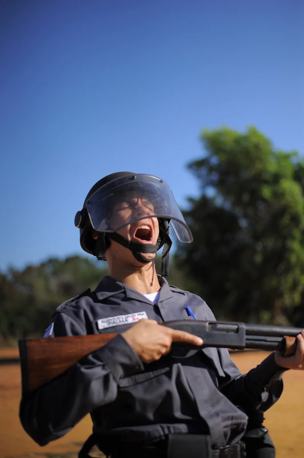 Aluna soldado da PMES em treinamento de choque com capacete e espingarda, expressão intensa de garra durante exercício