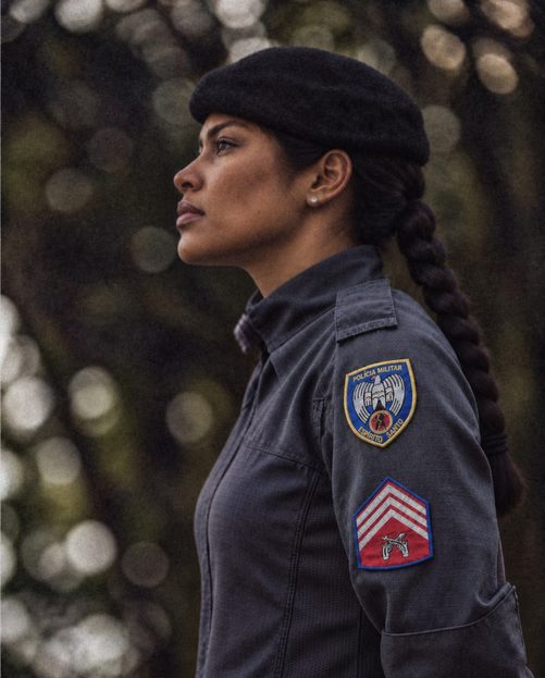 Aluna sargento de perfil, de boina, com a divisa de sargento na manga do uniforme.